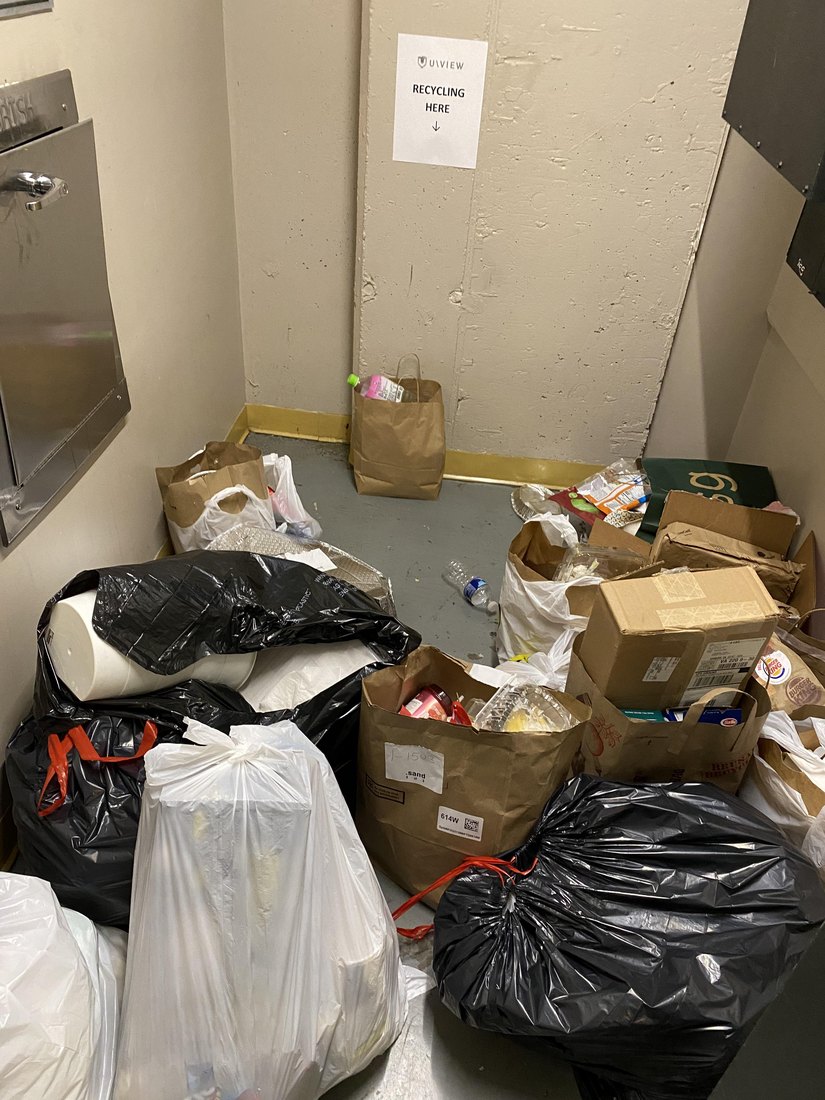A waste chute room with rubbish bags and loose waste piled on the floor.